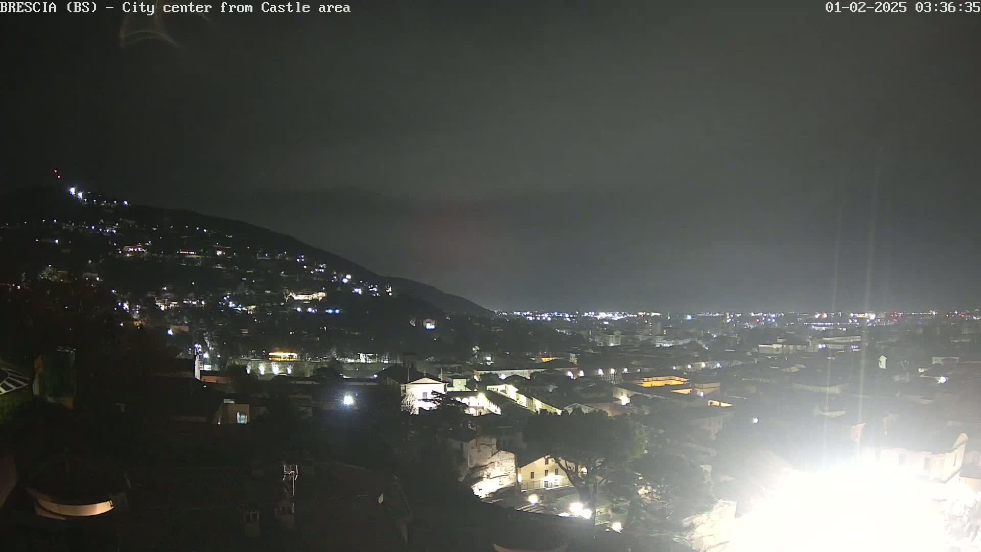 A nighttime view of a city nestled against a hill, under a dark, overcast sky.