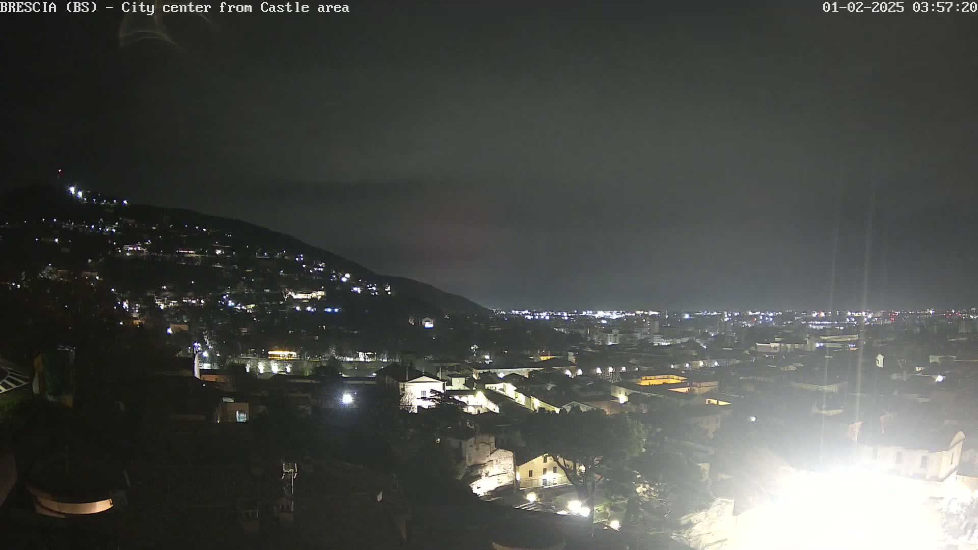 A nighttime view of a city nestled against a hill, under a dark, overcast sky.