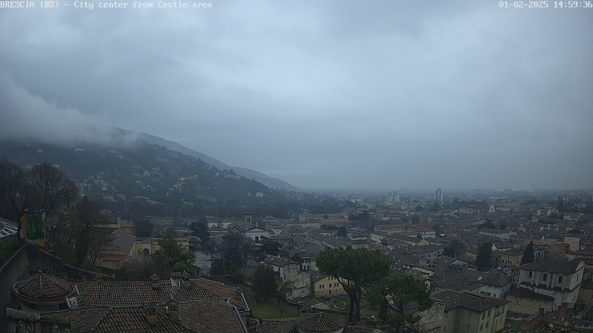 A hazy, overcast day reveals a sprawling city nestled in a valley, with a hill shrouded in fog in the background.