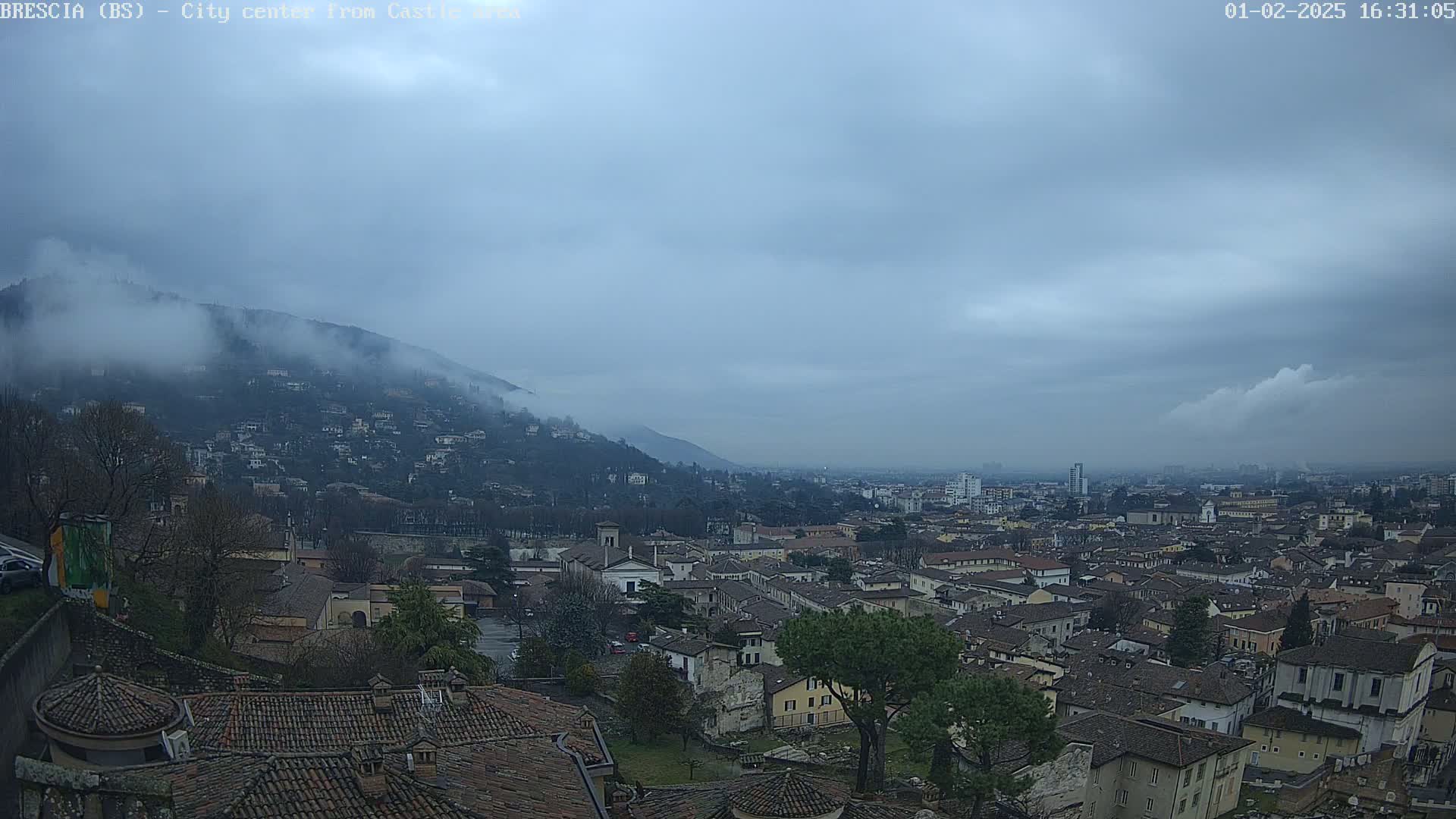 A sprawling city nestled below a fog-covered mountain under a cloudy sky.