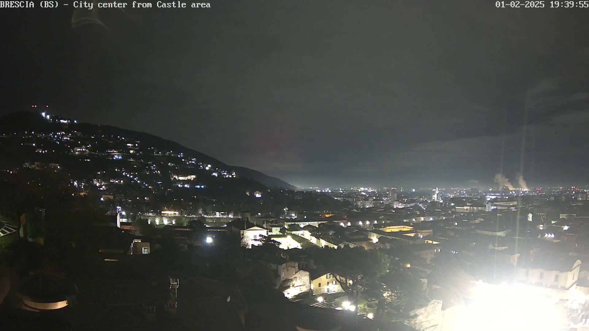 A nighttime view of a city nestled against a hillside under a dark, overcast sky.
