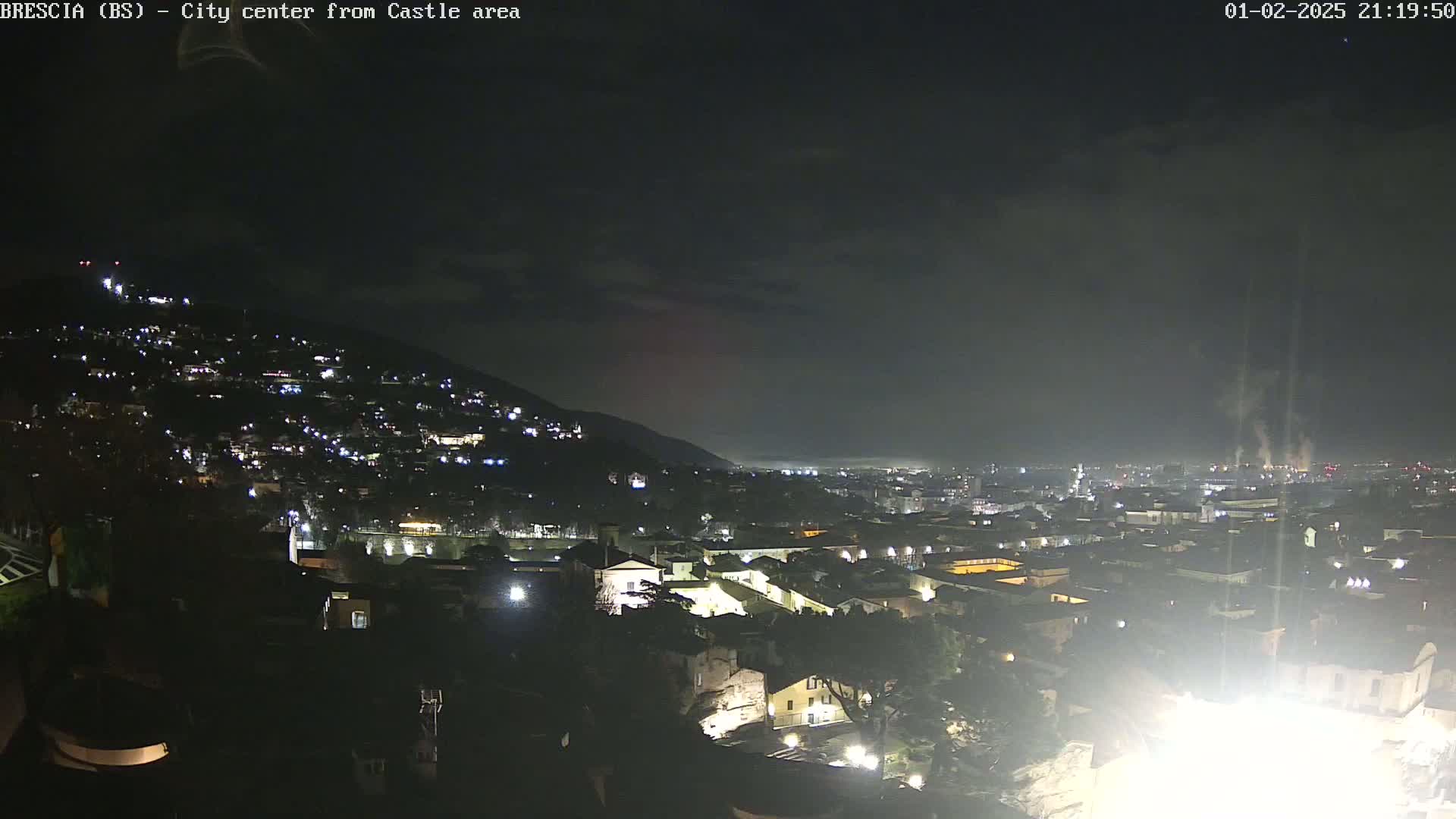 A nighttime view of a city nestled against a hill, under a dark, cloudy sky.