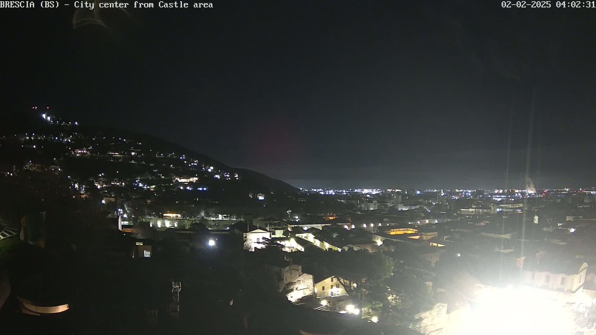 A nighttime view of a city illuminated by lights, situated on a hillside under a clear, dark sky.