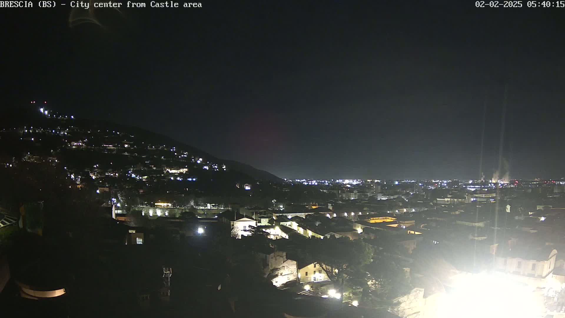 A nighttime view of a city nestled against a hill, illuminated by scattered lights under a dark, clear sky.
