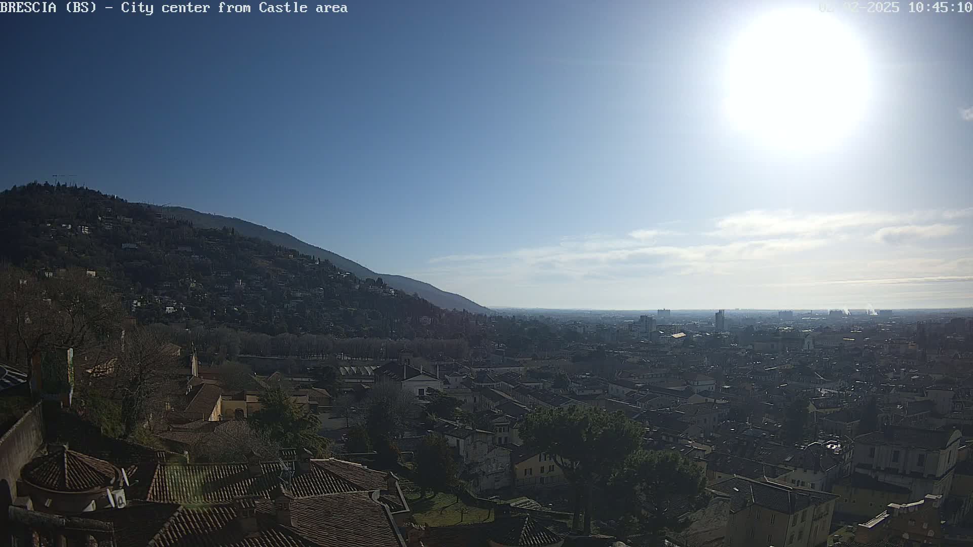 A sunny day reveals a sprawling city vista from a hilltop vantage point, with a mountain in the background.