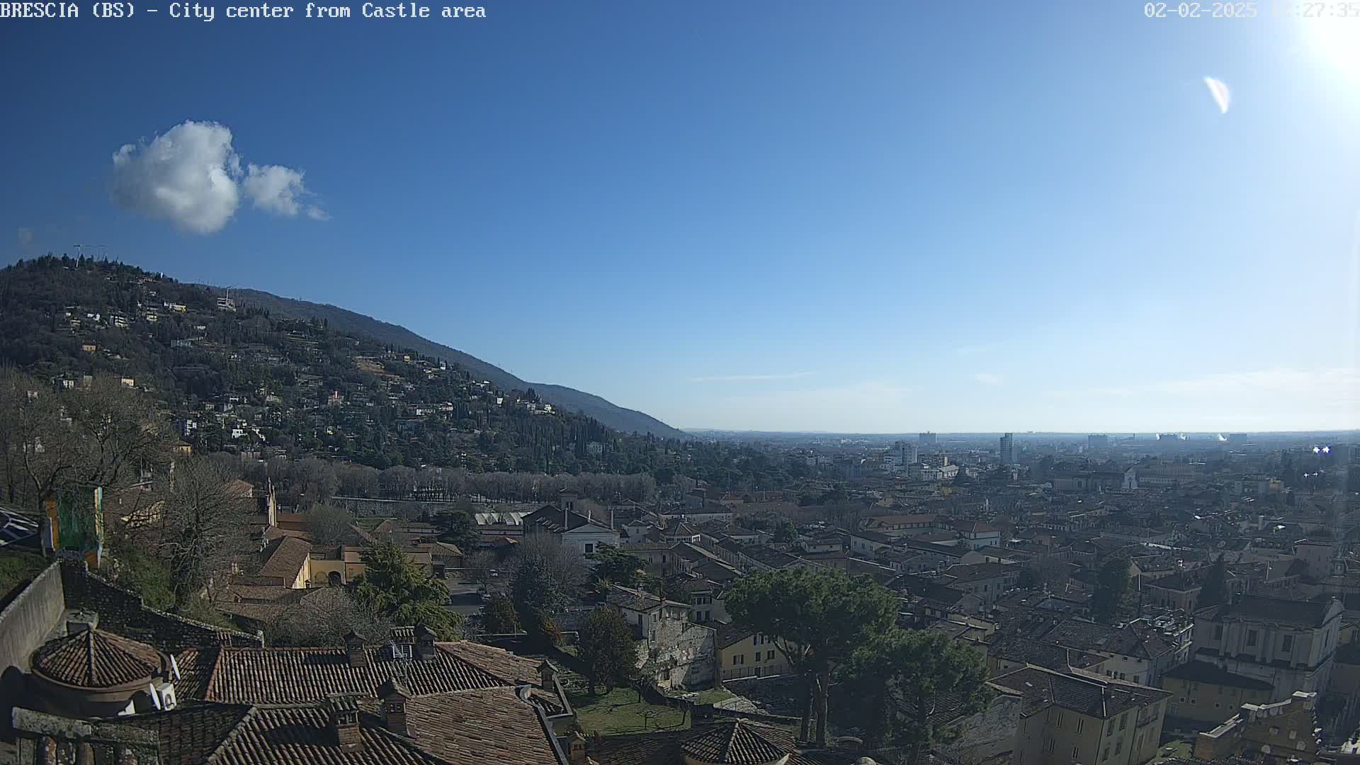 A sprawling city with red-tiled roofs nestles beneath a hill on a clear, sunny day.