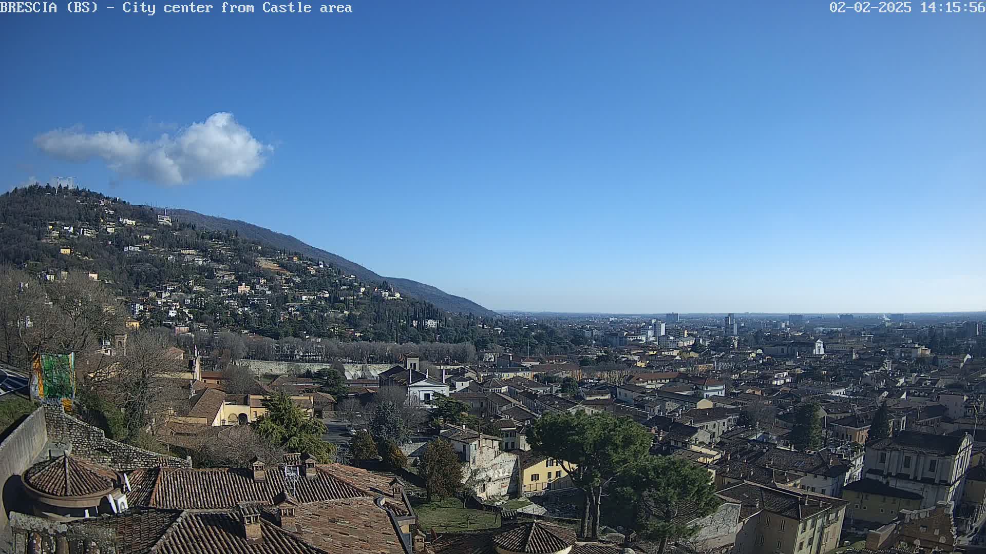 A sunny day reveals a sprawling city nestled at the base of a hill, with a single cloud in the otherwise clear blue sky.