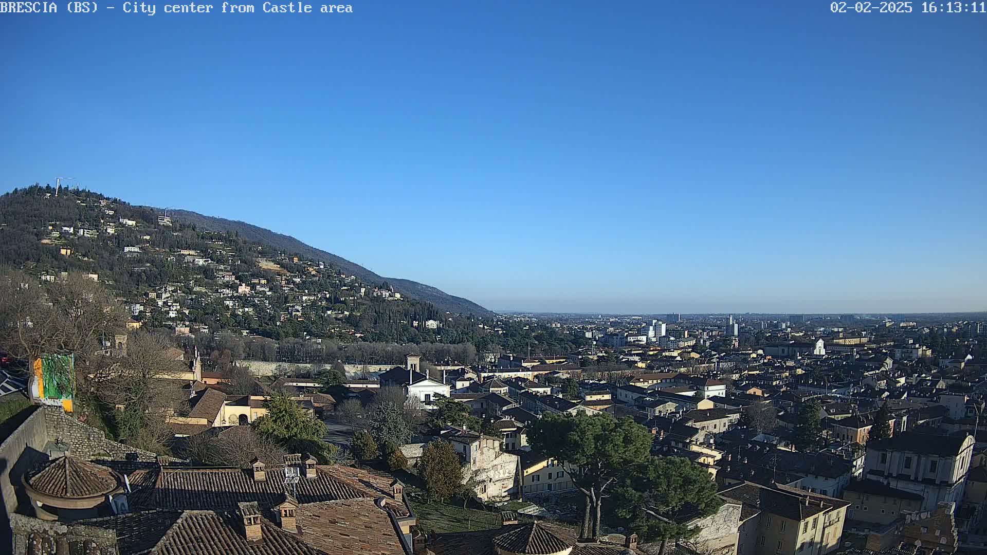A sprawling city nestled beneath a clear blue sky and a hillside covered in buildings and trees.