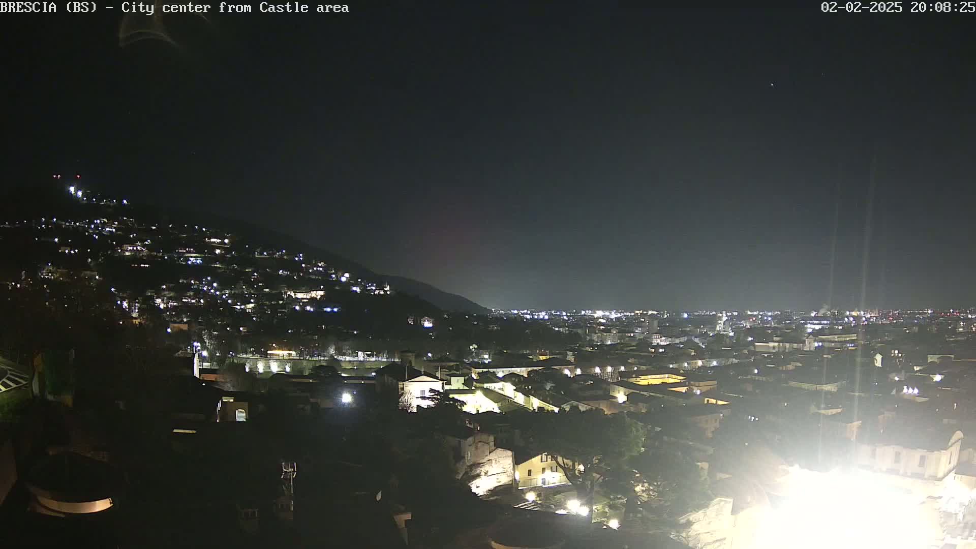A nighttime view of a city nestled against a hill, illuminated by numerous lights under a clear, dark sky.