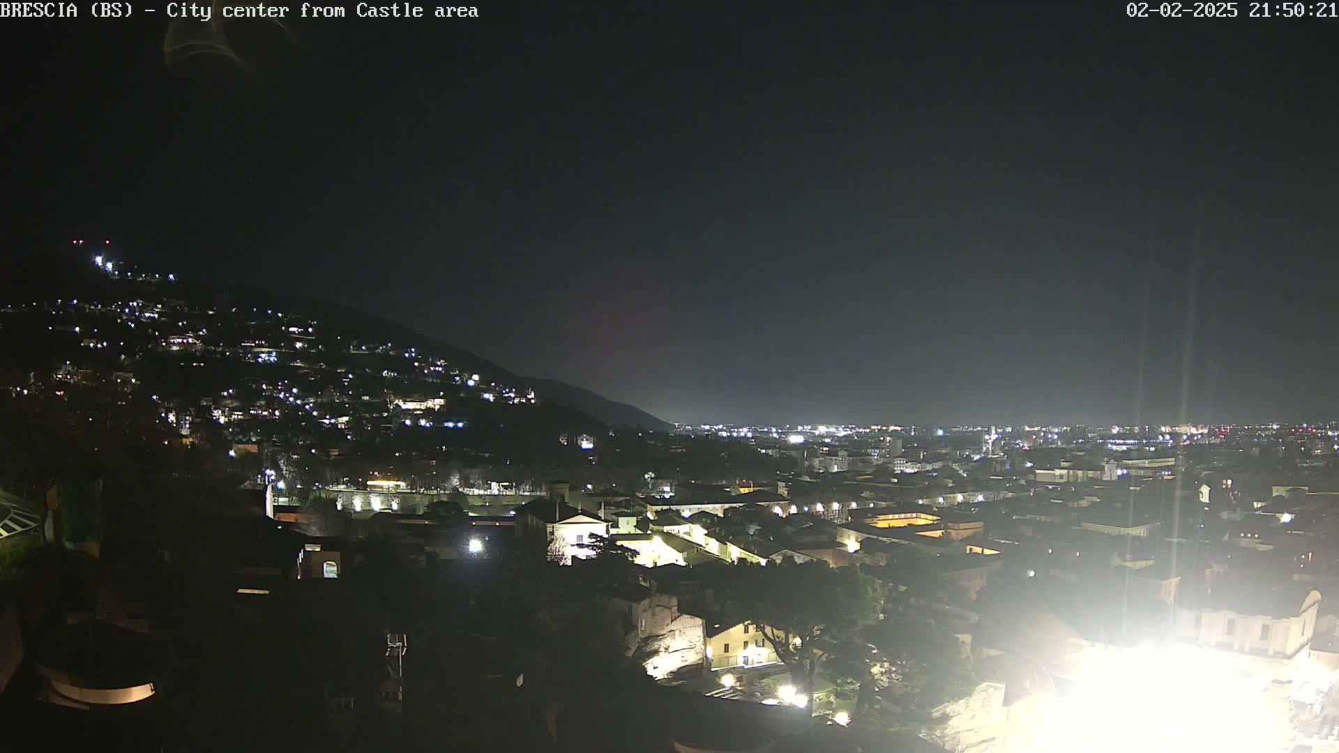 A nighttime view shows a city illuminated by lights on a hillside, extending to a darker plain in the distance under a clear, dark sky.
