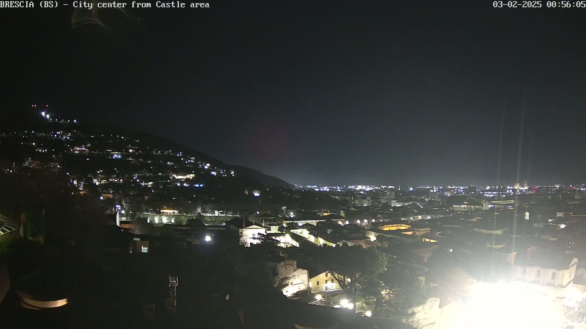 A nighttime view of a city nestled against a hill, illuminated by numerous lights under a clear, dark sky.
