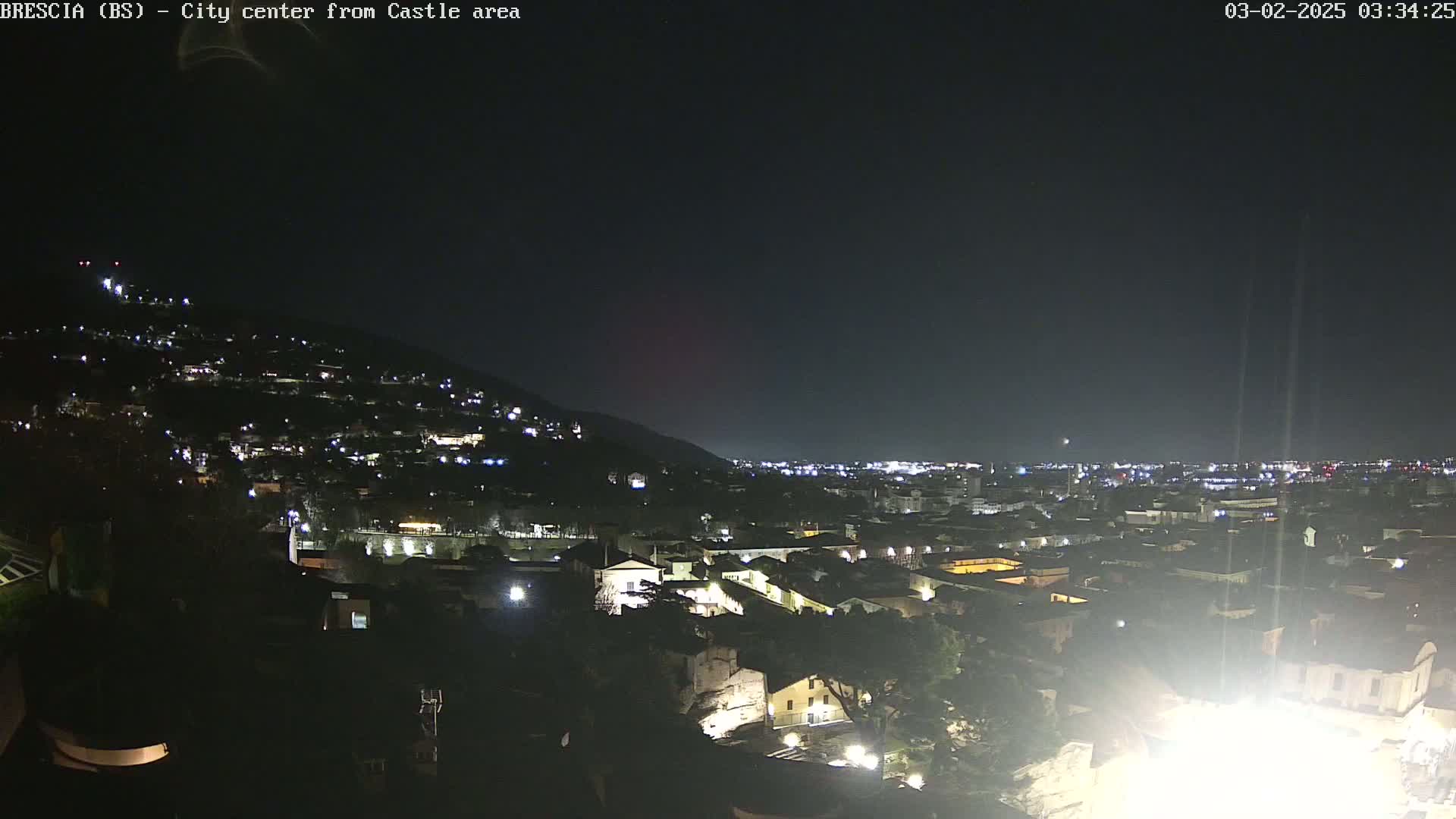 A nighttime view of a city nestled against a hill, illuminated by scattered lights under a dark, clear sky.