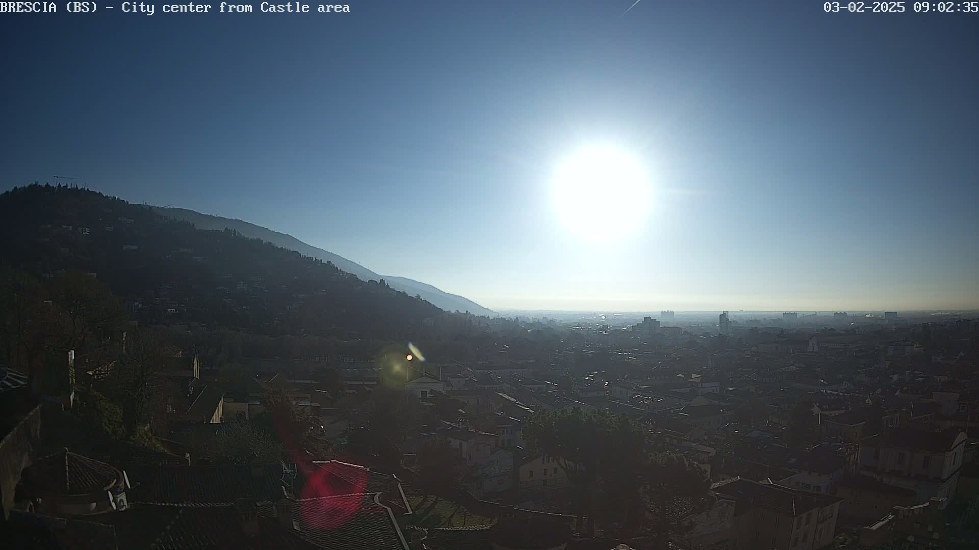 A sunny day reveals a hazy view of a city nestled in a valley, with mountains in the background.