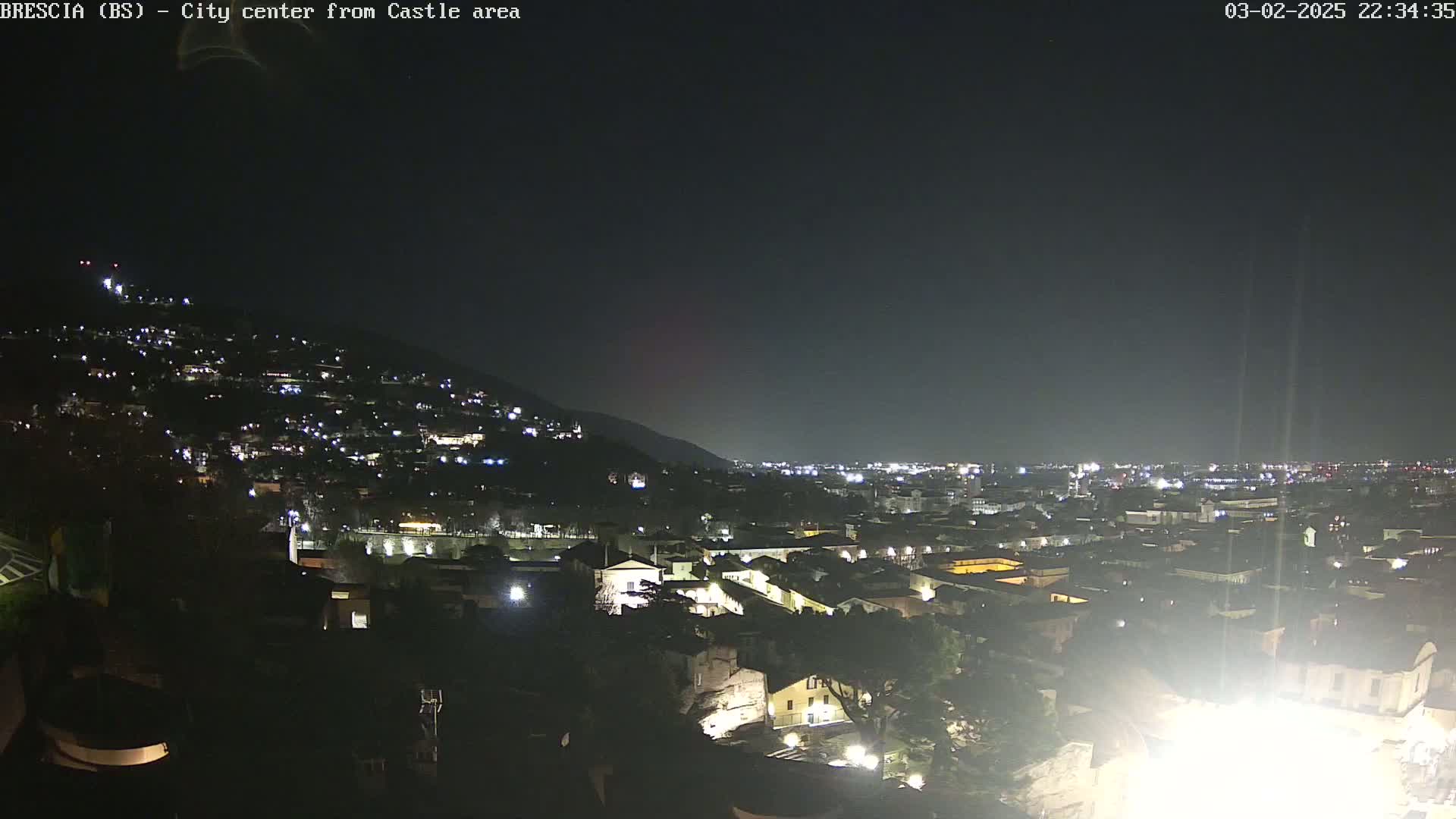 A nighttime view of a city illuminated by lights, nestled against a dark hill under a clear, dark sky.