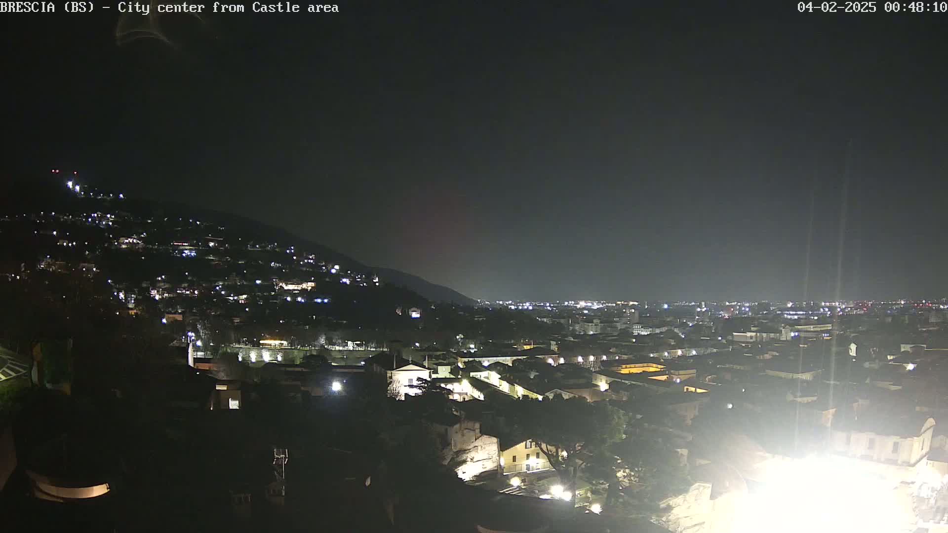 A nighttime, aerial view of a city nestled against a hill, with many lights illuminating buildings and streets under a dark sky.