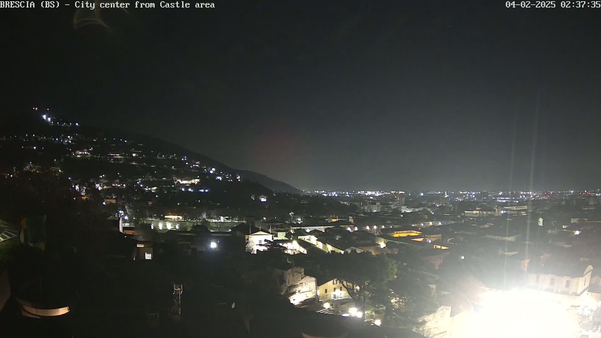 A nighttime long shot of a city on a hillside, illuminated by scattered lights under a clear, dark sky.