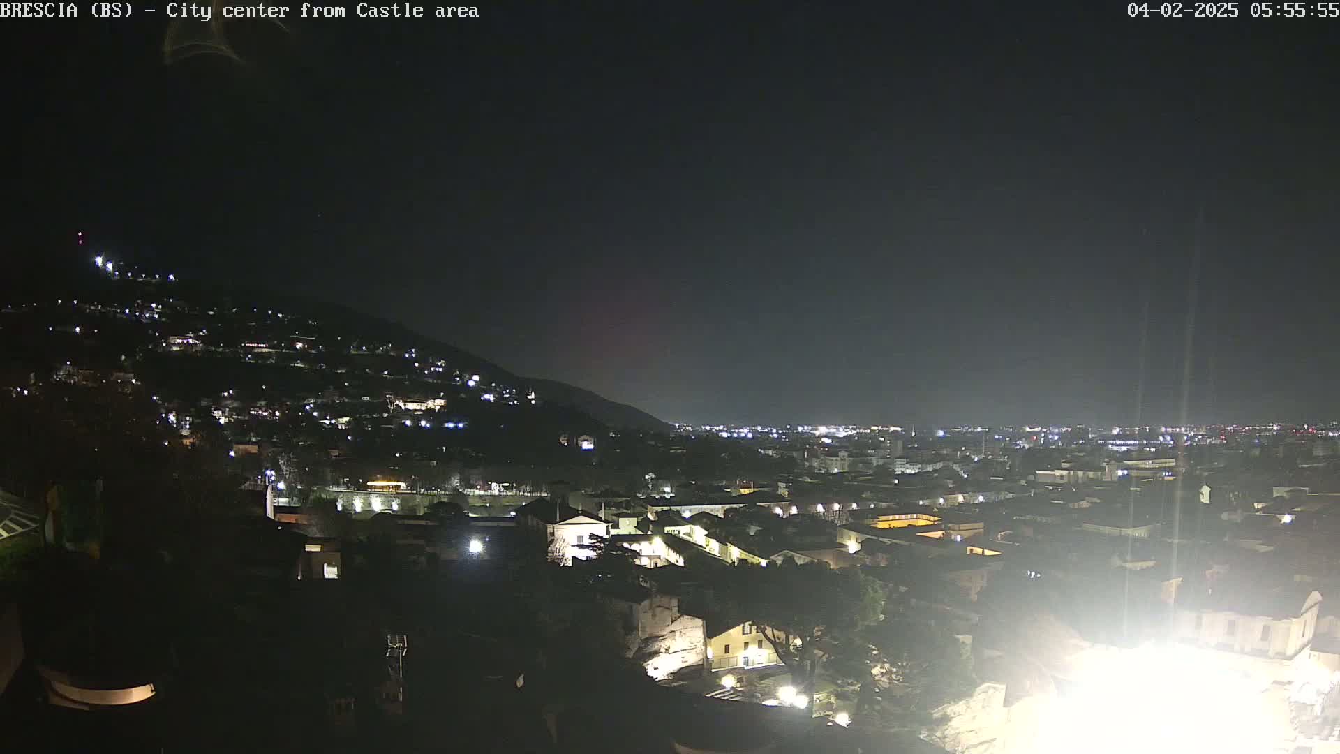 A nighttime view of a city nestled against a hillside, under a clear, dark sky.