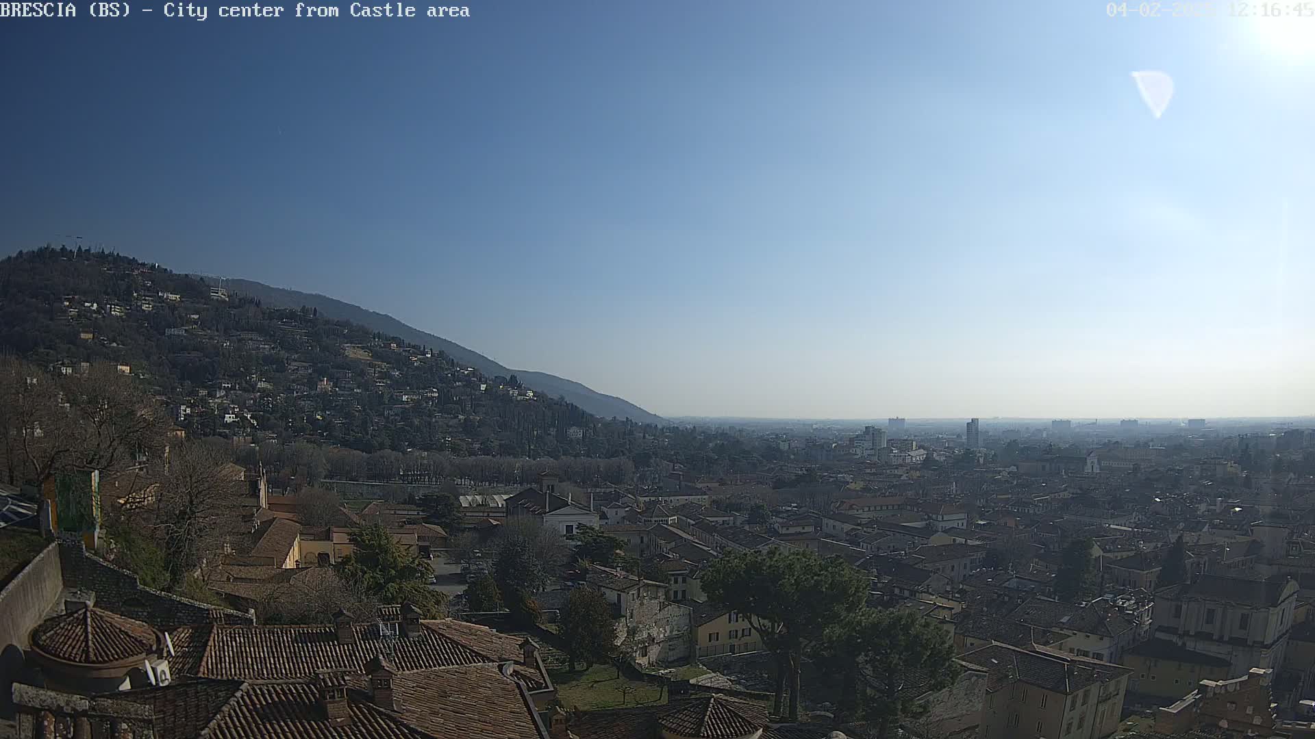 A sunny, clear day reveals a sprawling city nestled between a hillside and a distant plain.