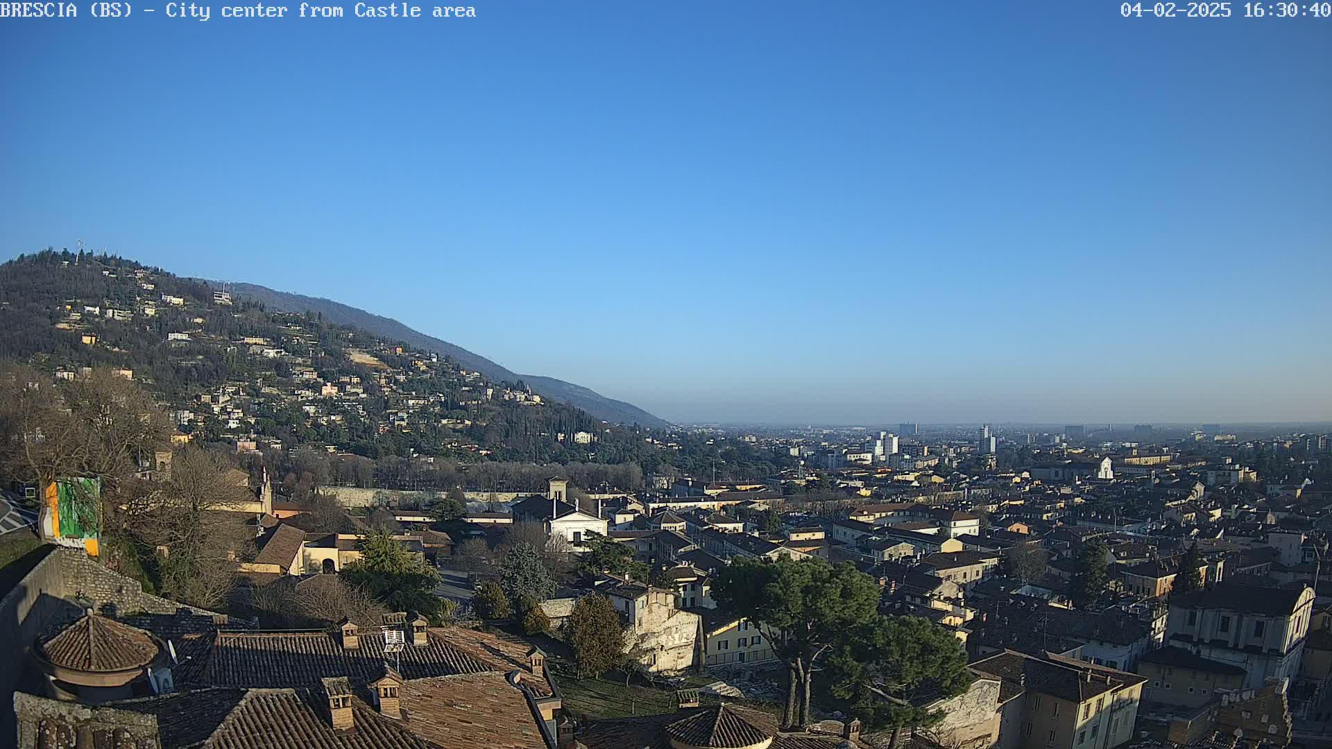 A sprawling city with terracotta rooftops nestled against a hillside, under a clear blue sky.