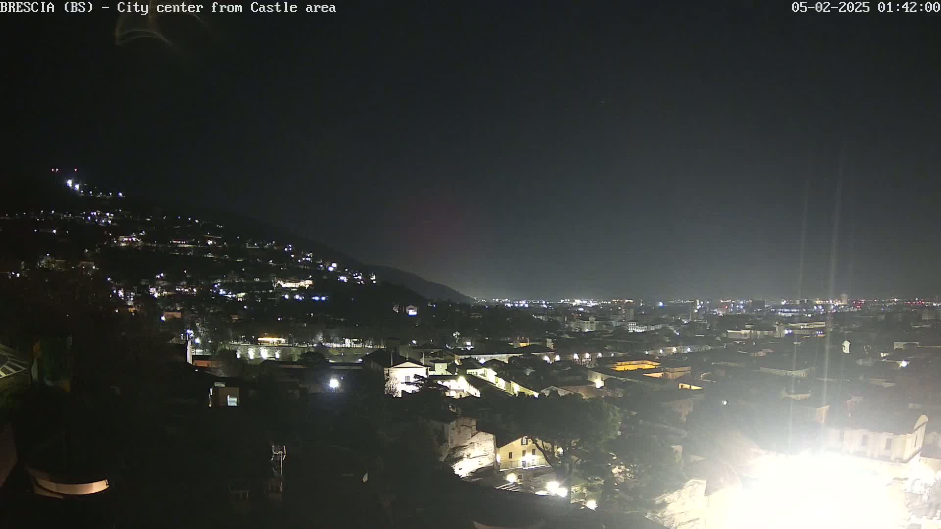 A nighttime view of a city nestled in a valley, illuminated by numerous lights, under a clear, dark sky.