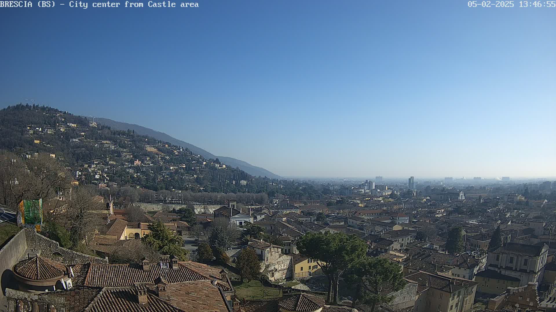 A sprawling city with red-tiled roofs nestled against a mountainside under a clear, blue sky.