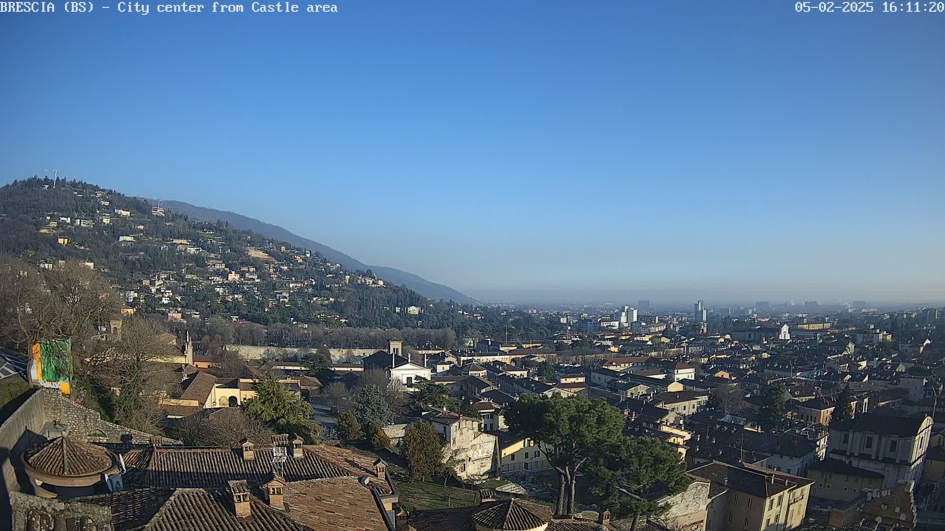 A sprawling city nestled against a hillside under a clear, bright blue sky.
