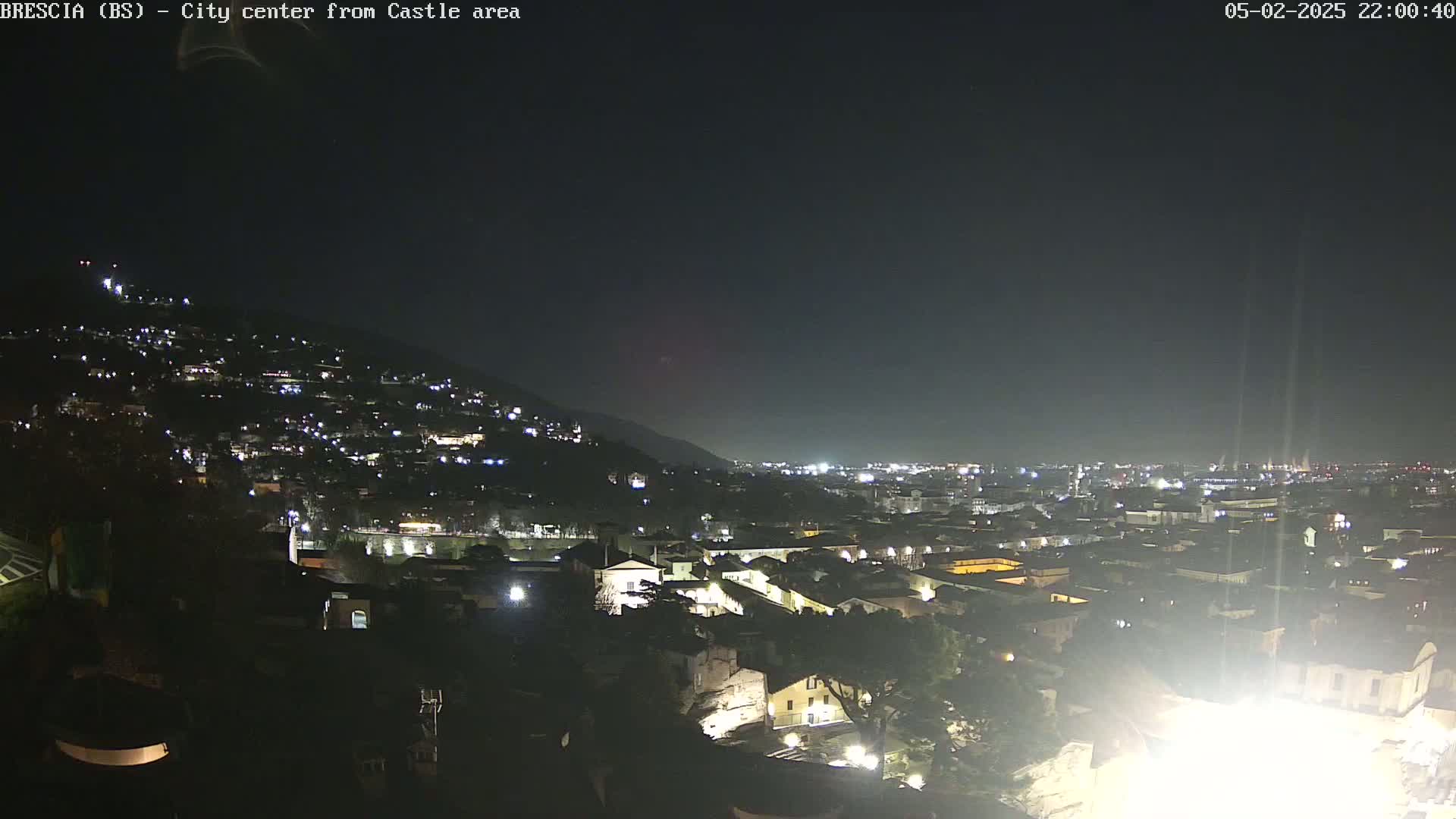 A nighttime, long shot of a city nestled in a valley, illuminated by the lights of buildings on a hill and in the distance under a dark sky.