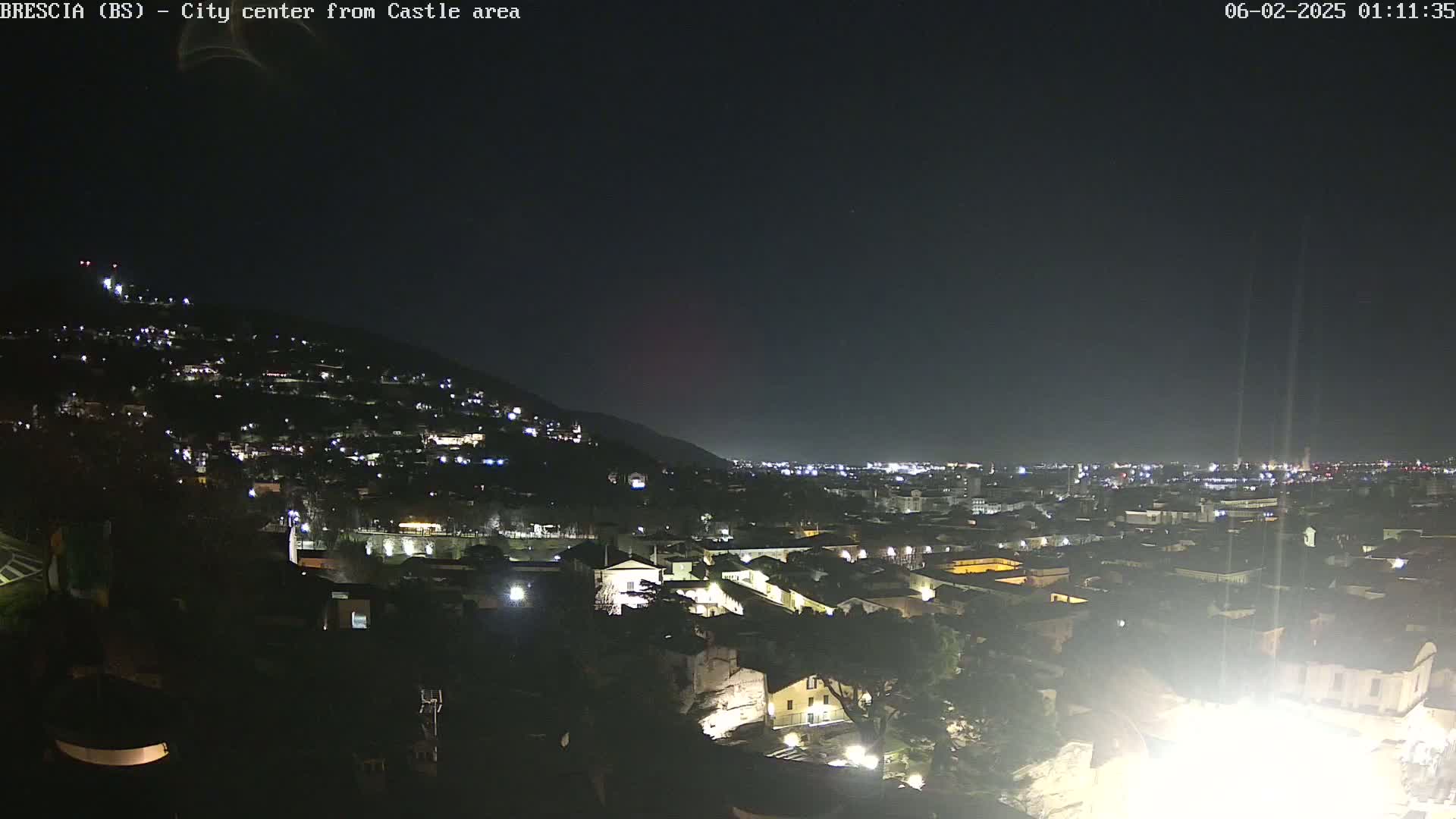 A nighttime view of a city nestled against a hillside, illuminated by scattered lights under a clear, dark sky.