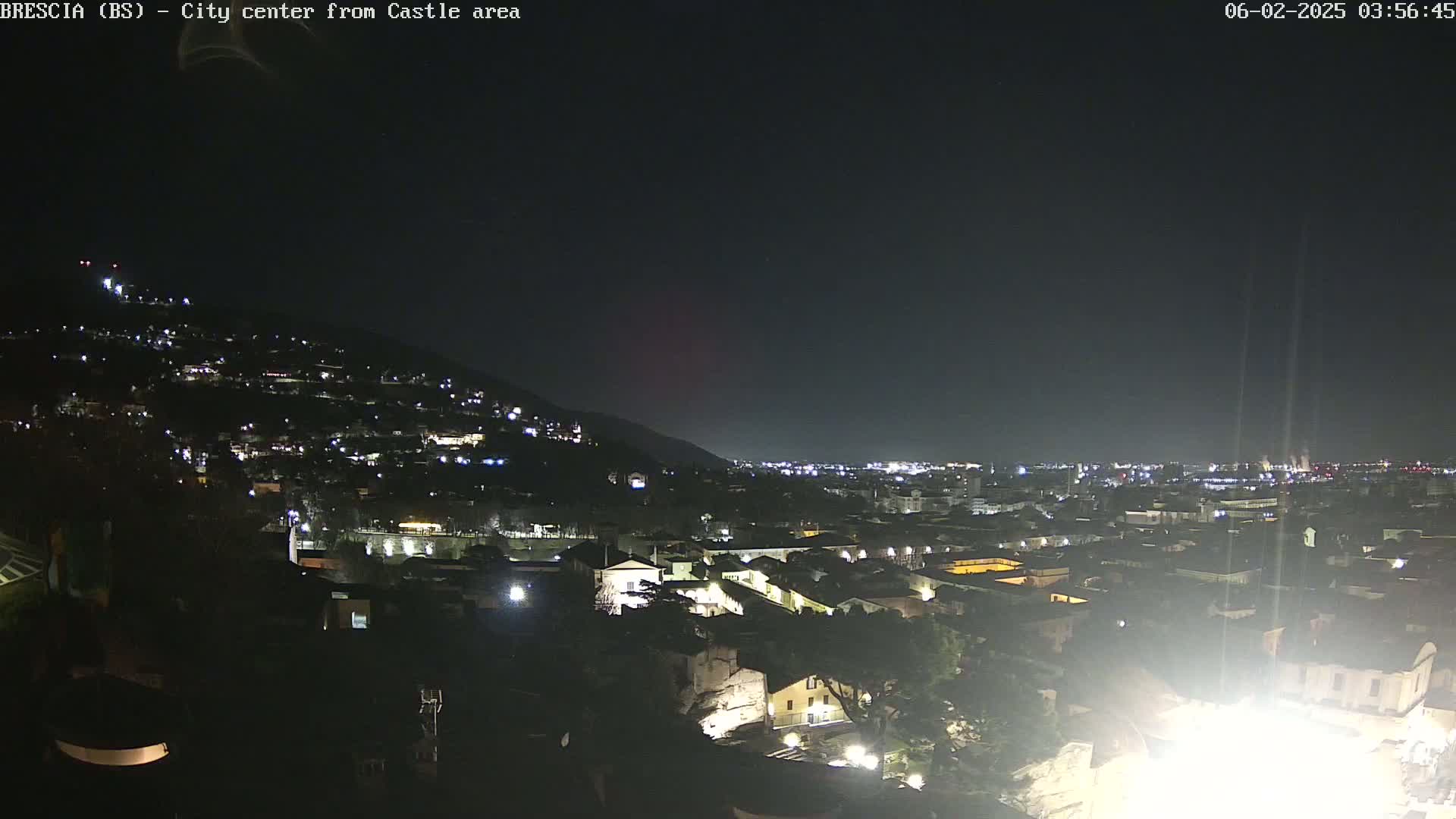 A nighttime, long shot of a city nestled against a hill, illuminated by scattered lights under a clear, dark sky.