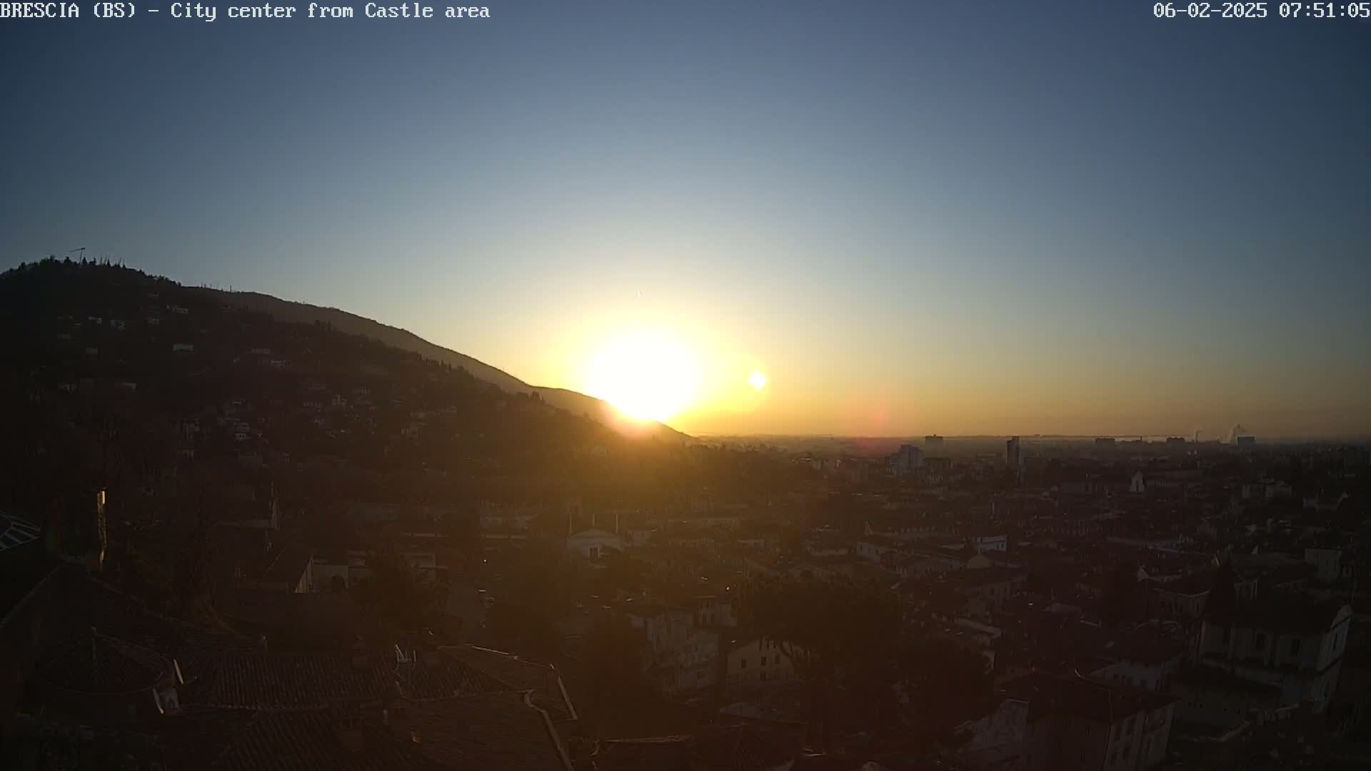 A hazy sunrise illuminates a city nestled in a valley, with hills rising in the background.
