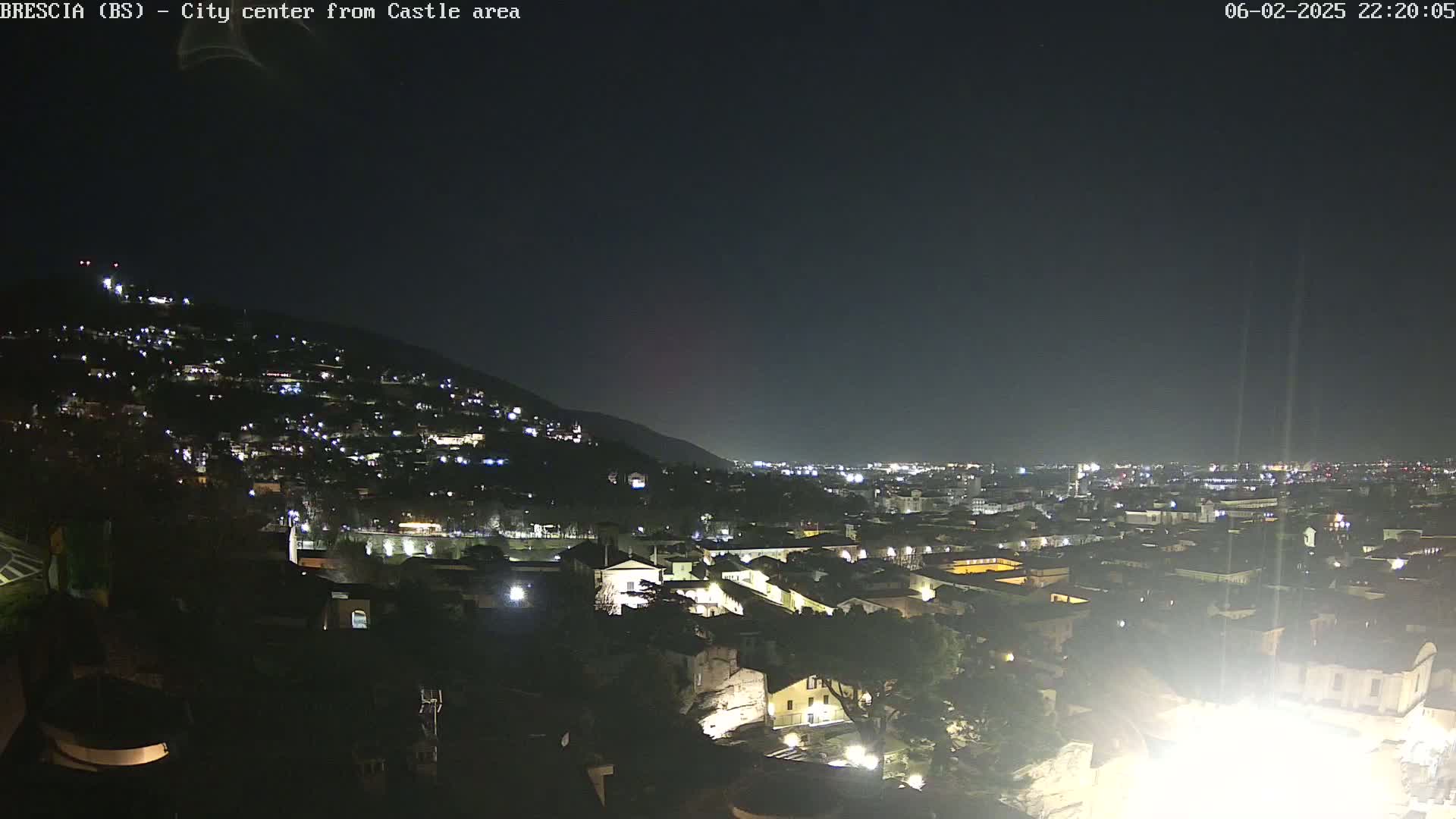 A nighttime view shows a city illuminated by lights spread across a hillside and a flat plane, under a dark, clear sky.