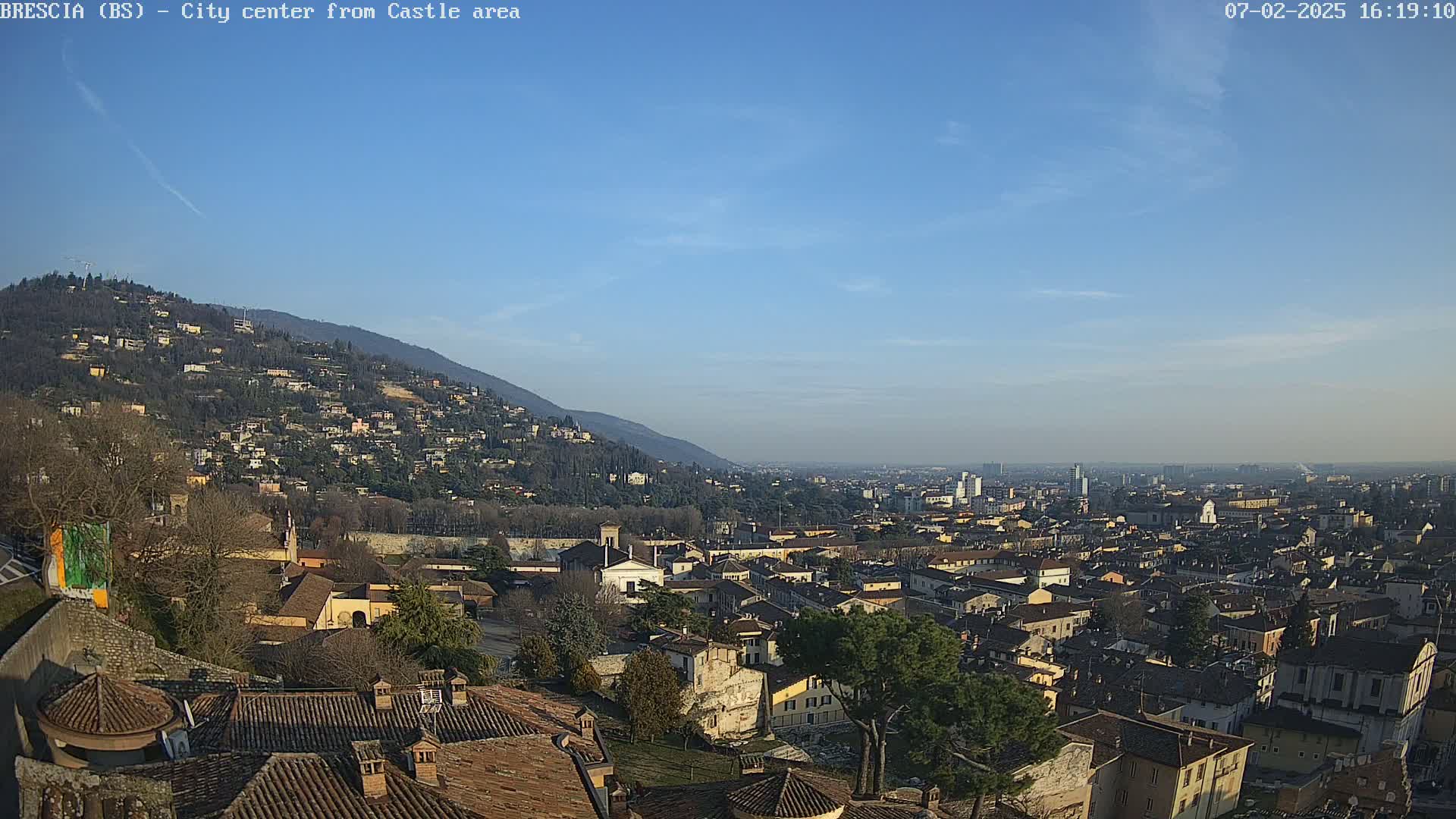 A sprawling city nestled against a hillside under a clear blue sky.