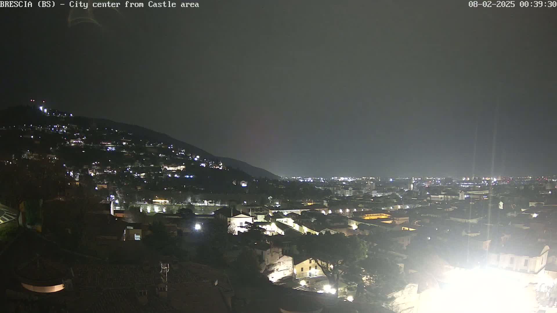 A nighttime view of a city nestled into a hillside, under a dark, overcast sky.