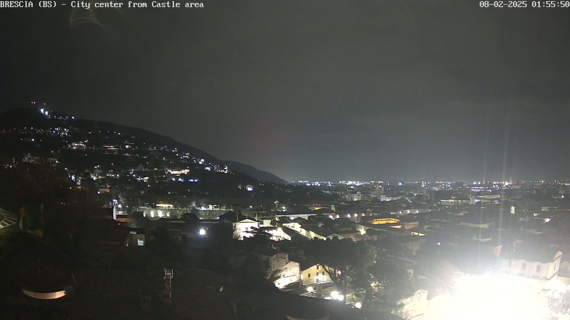 A nighttime view of a city sprawling across a hill and into a valley, under a dark, overcast sky.