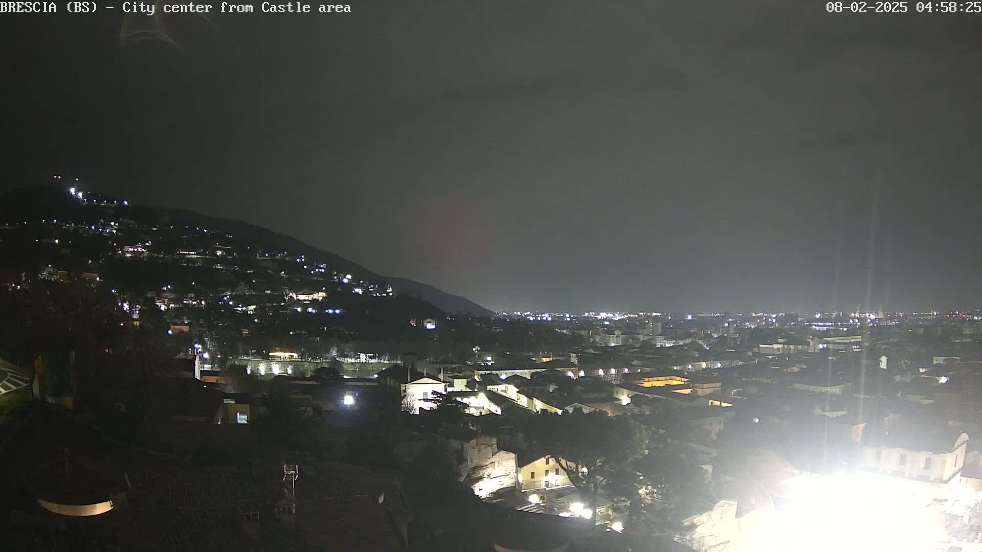 A nighttime view of a city nestled against a hillside, under a dark, overcast sky.
