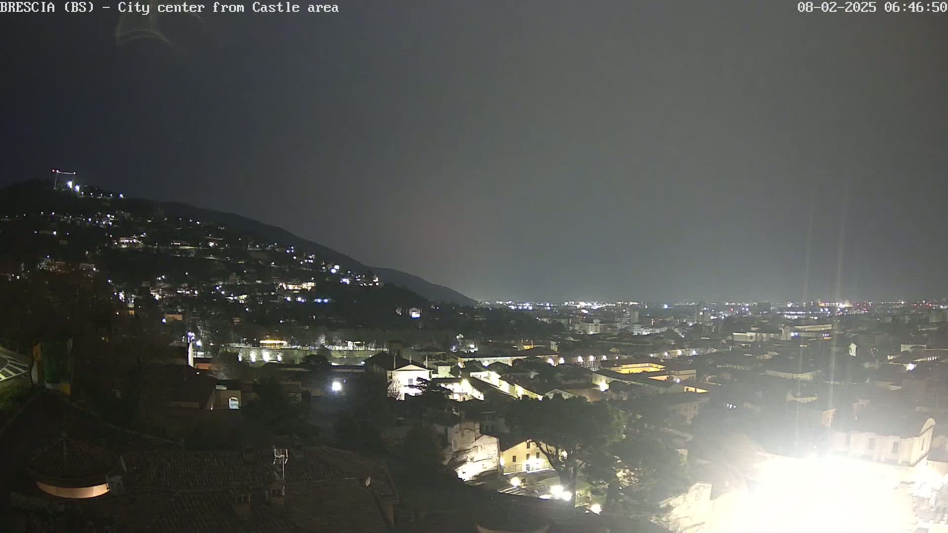 A nighttime view of a city nestled against a hillside under a dark, overcast sky.