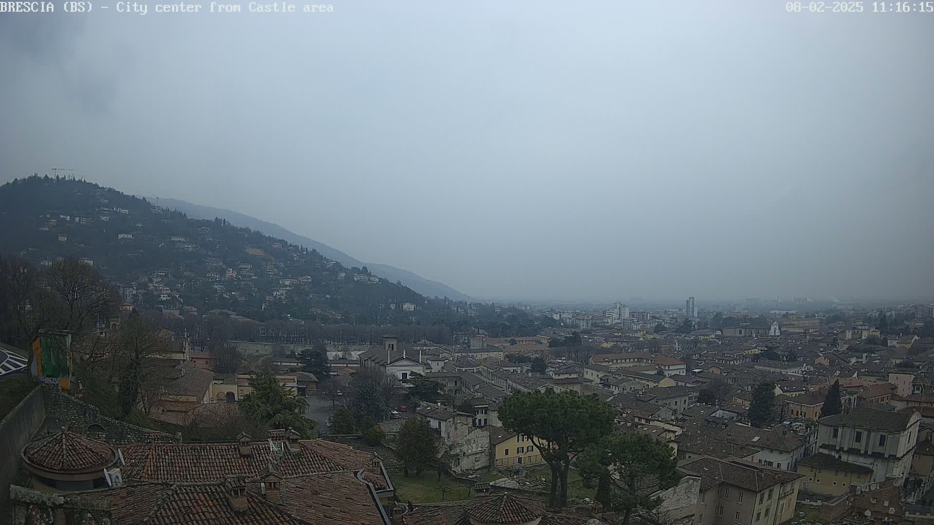 A hazy view from a hilltop shows a sprawling city of low-rise buildings nestled at the foot of a mountain.