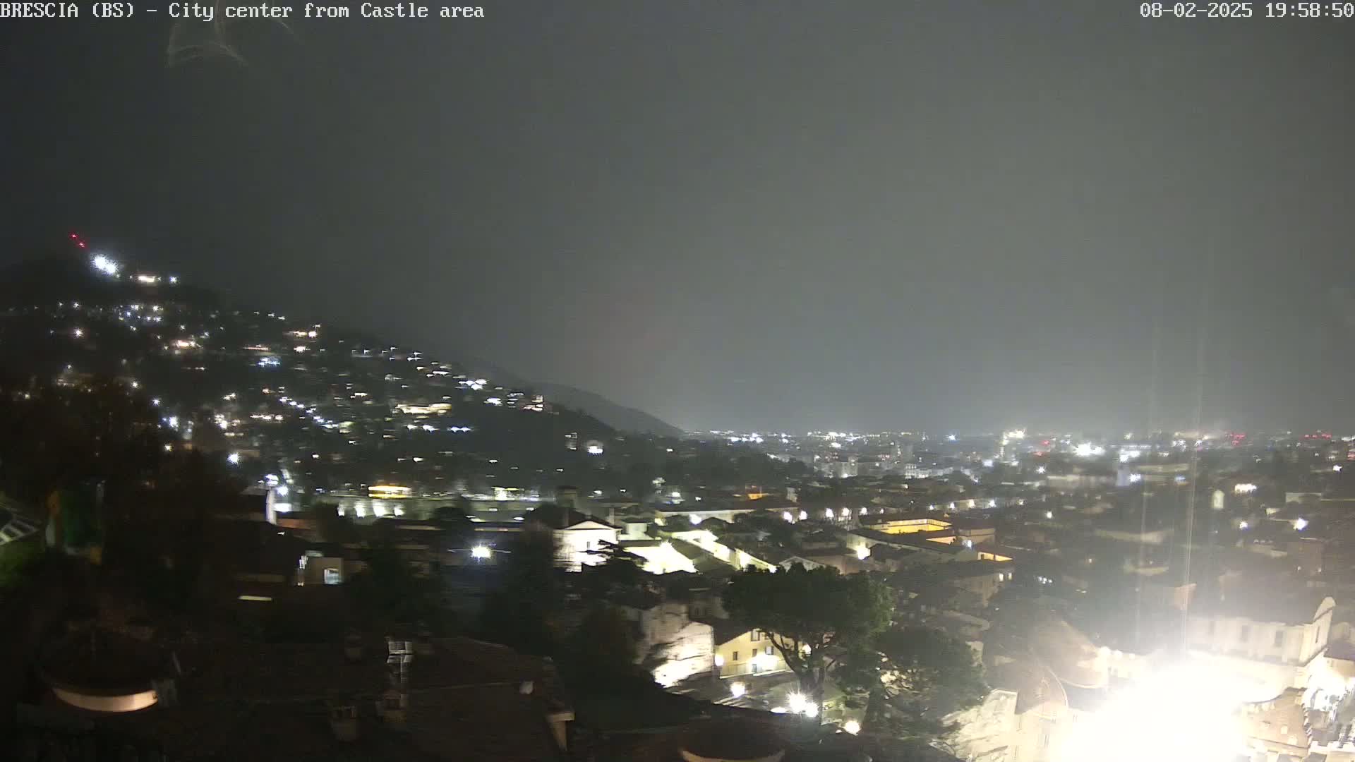 A nighttime view of a city sprawling across a hillside under a hazy, possibly rainy sky.