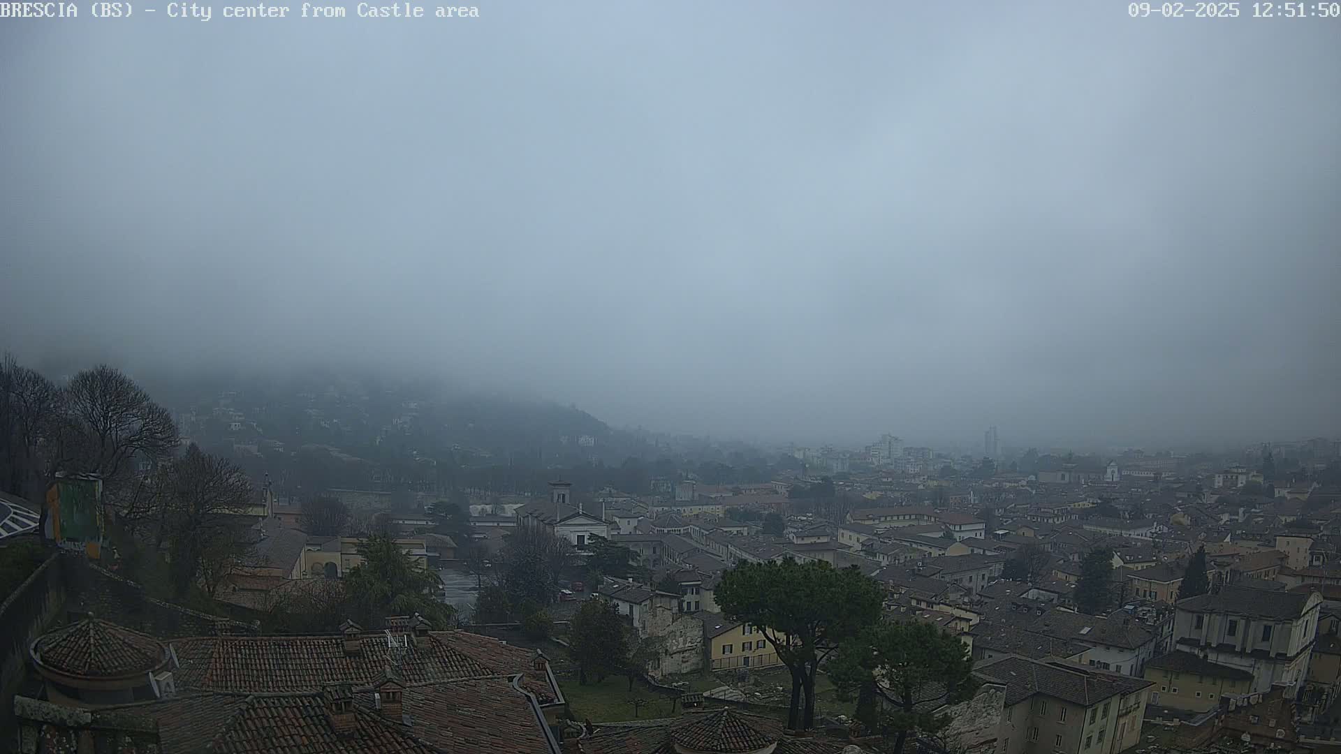 A foggy city view shows many buildings with red-tiled roofs extending to the horizon,  seen from a high vantage point.