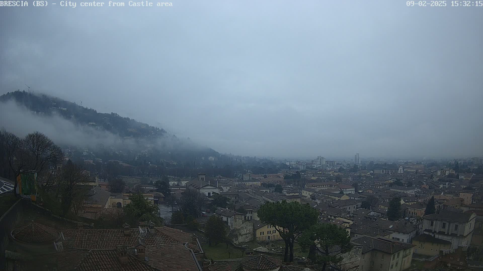 A foggy cityscape reveals a sprawling town nestled beneath a cloud-covered hill.