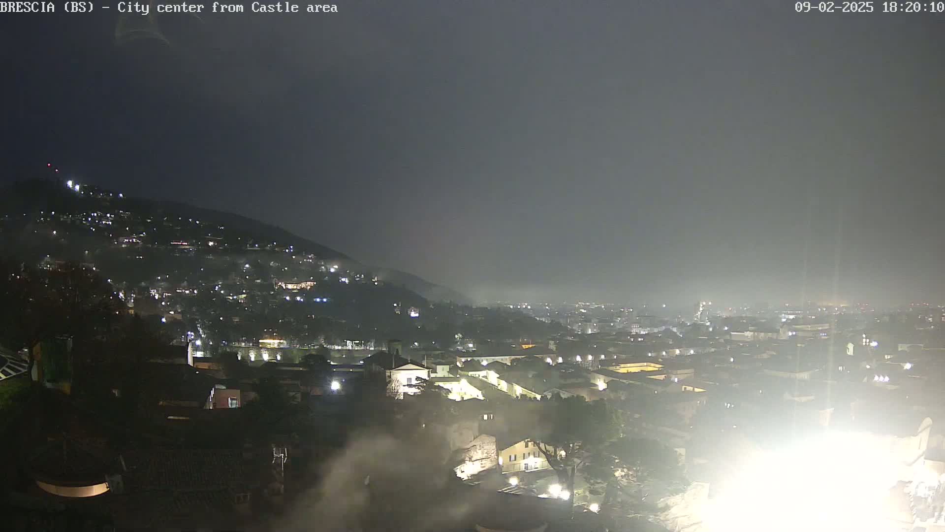 A nighttime view of a city nestled against a hill, shrouded in hazy atmospheric conditions.