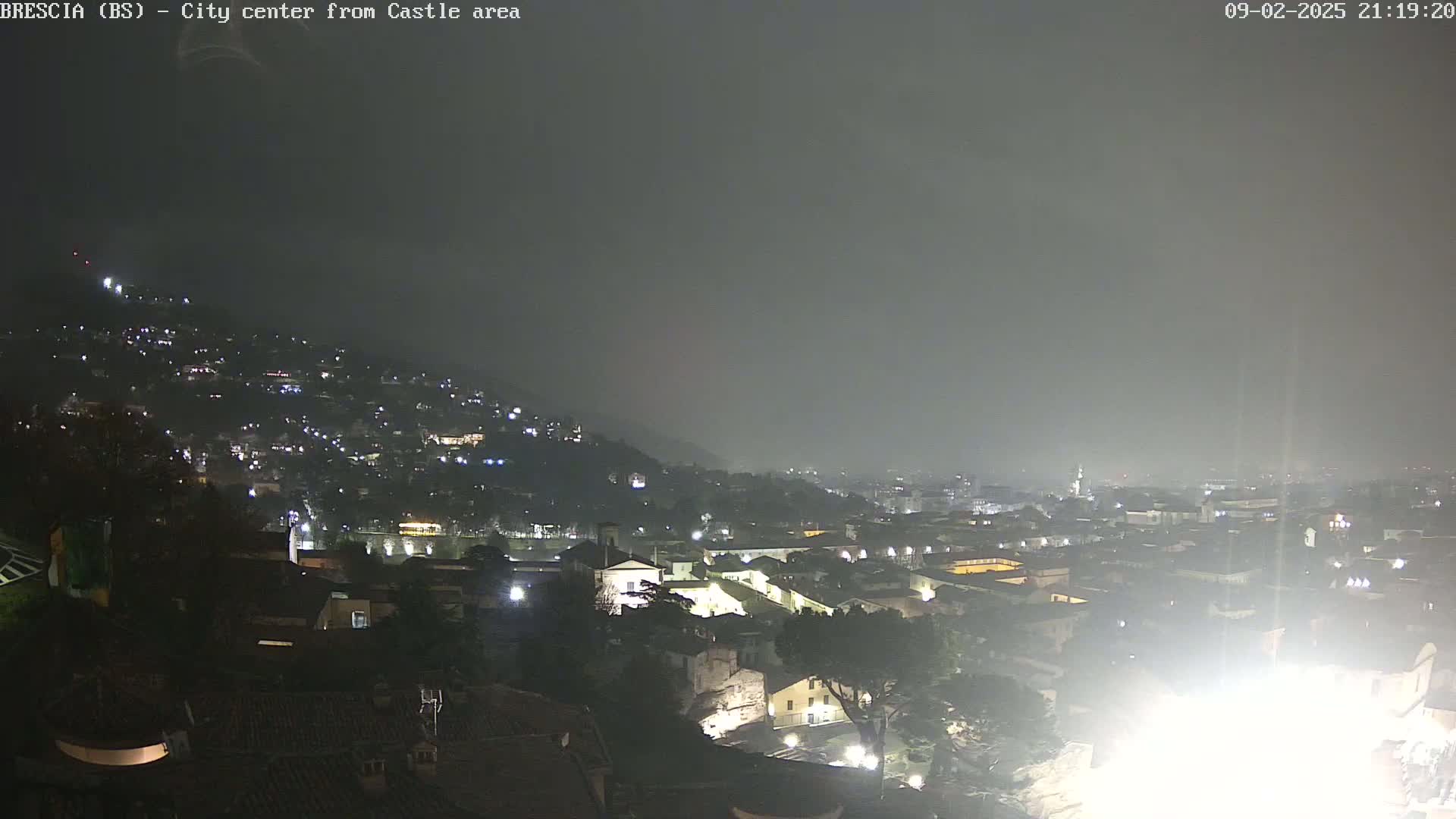 A nighttime, hazy view of a city nestled in a hillside, illuminated by scattered lights.