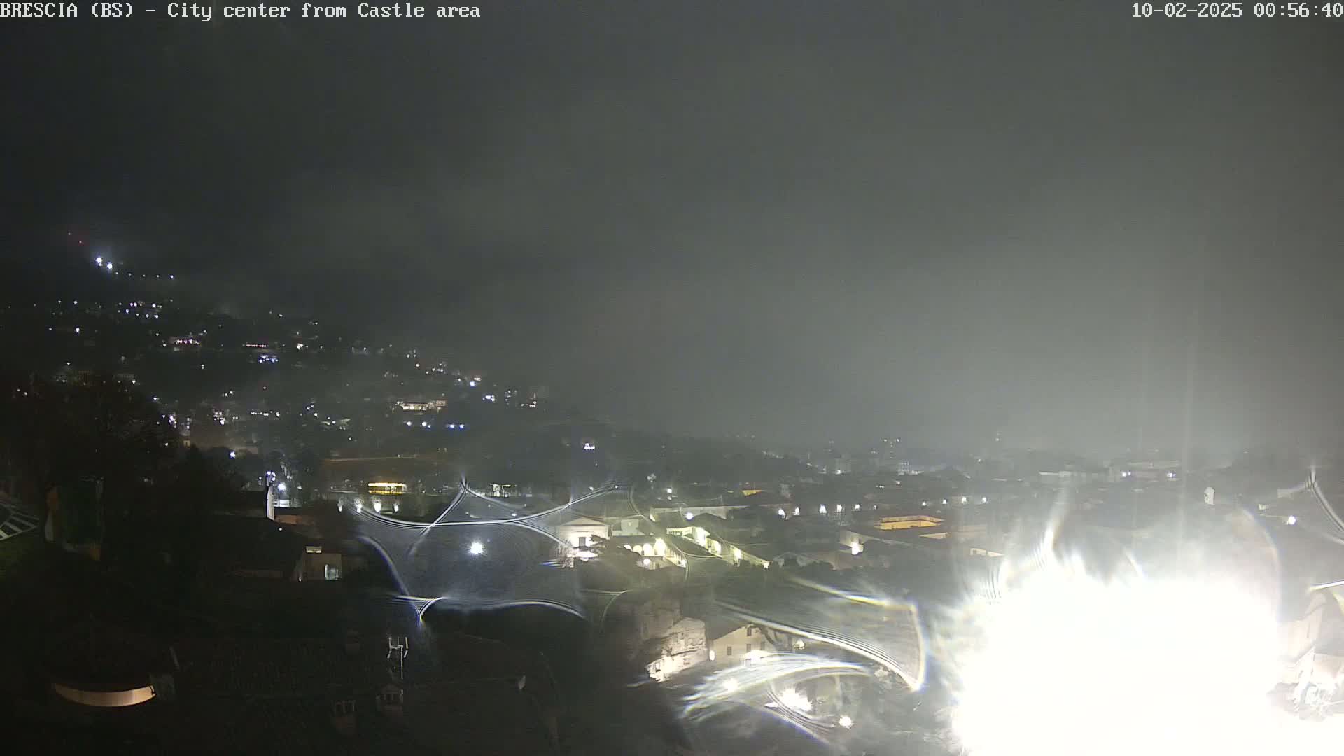 A nighttime, foggy view of a city illuminated by scattered lights, seen from an elevated vantage point.