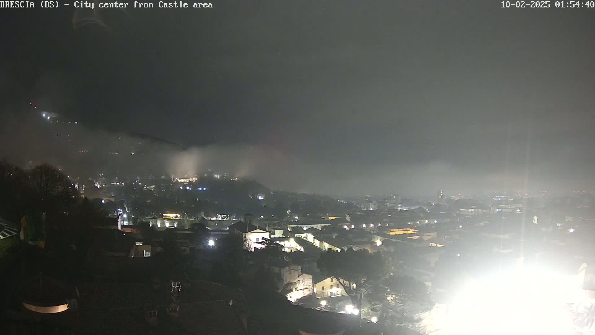 A nighttime view of a city shrouded in fog, with lights illuminating buildings and streets below.