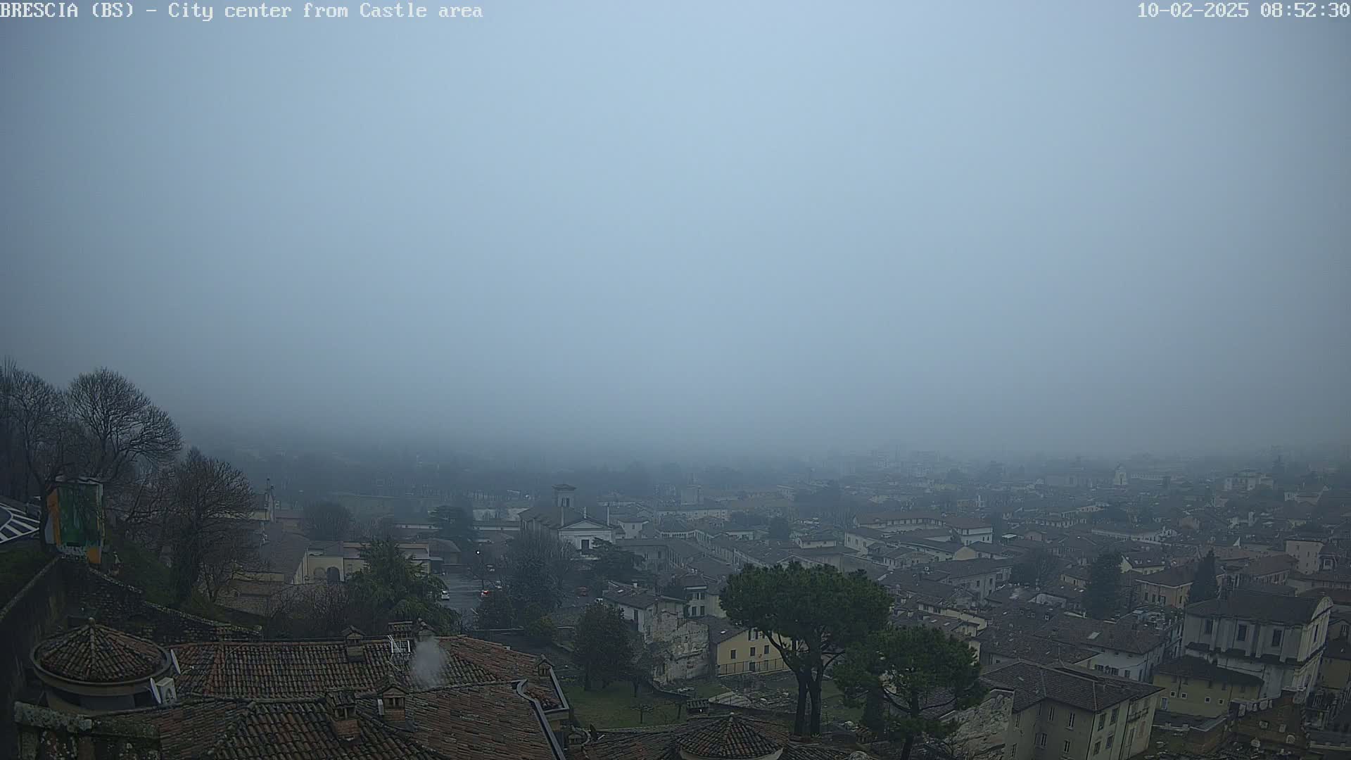 A foggy view of a city, seen from a higher vantage point, shows many buildings with red tile roofs.