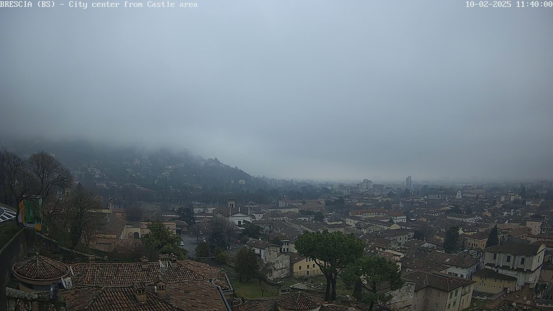 A foggy cityscape, viewed from an elevated position, shows a sprawling expanse of buildings and hills shrouded in mist.