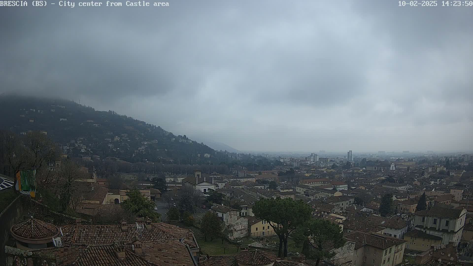 A sprawling city with numerous brown-roofed buildings nestled at the base of a hill under an overcast sky.