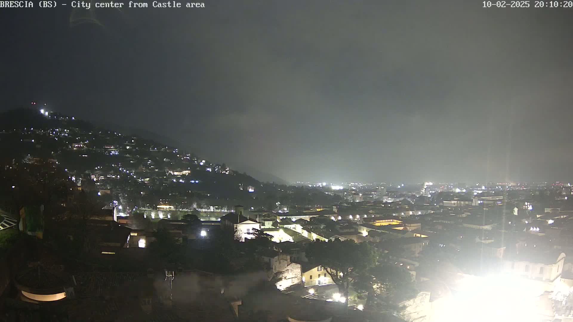 A nighttime view of a city sprawling across a hillside under a cloudy sky.
