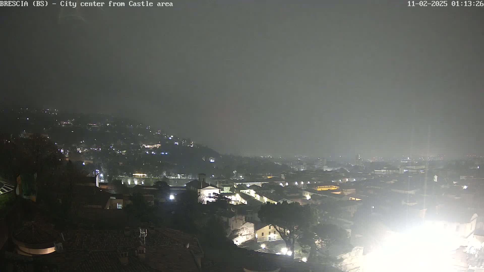 A night-time, hazy view of a city sprawling across a hillside, illuminated by scattered lights.