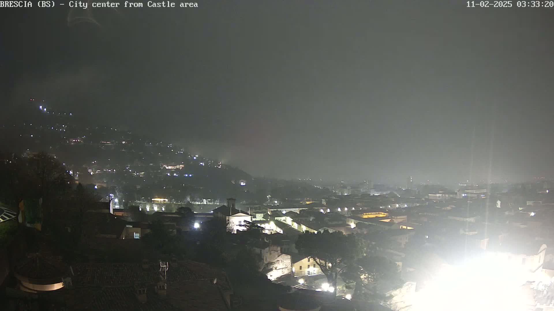 A nighttime view of a city shrouded in fog, with dimly lit buildings and hills visible in the distance.